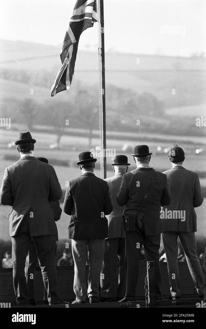 UK, England, Devonshire, Buckfastleigh, 1972. Point-to-Point races were held at  Dean Court on the Dean Marshes, close to the A38 between Plymouth and Exeter. Three stewards wearing black bowler hats in the center and other spectators watching a race under The Union Jack or Union Flag of the UK. Stock Photo