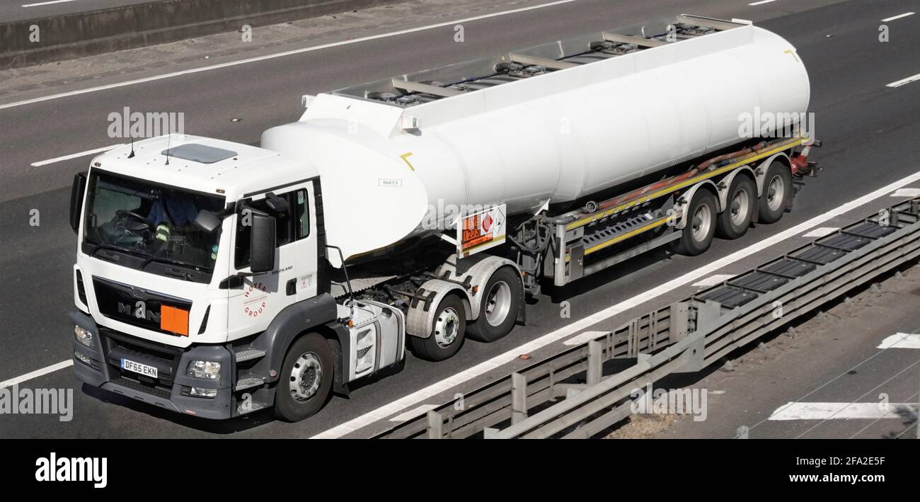 Front side & top view of white supply chain fuel delivery tanker trailer Hazchem chemical warning sign & MAN lorry truck UK motorway crash barrier Stock Photo