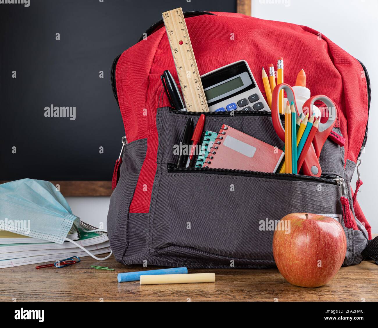 Book bag with school supplies on a desk with blank chalkboard in background Stock Photo