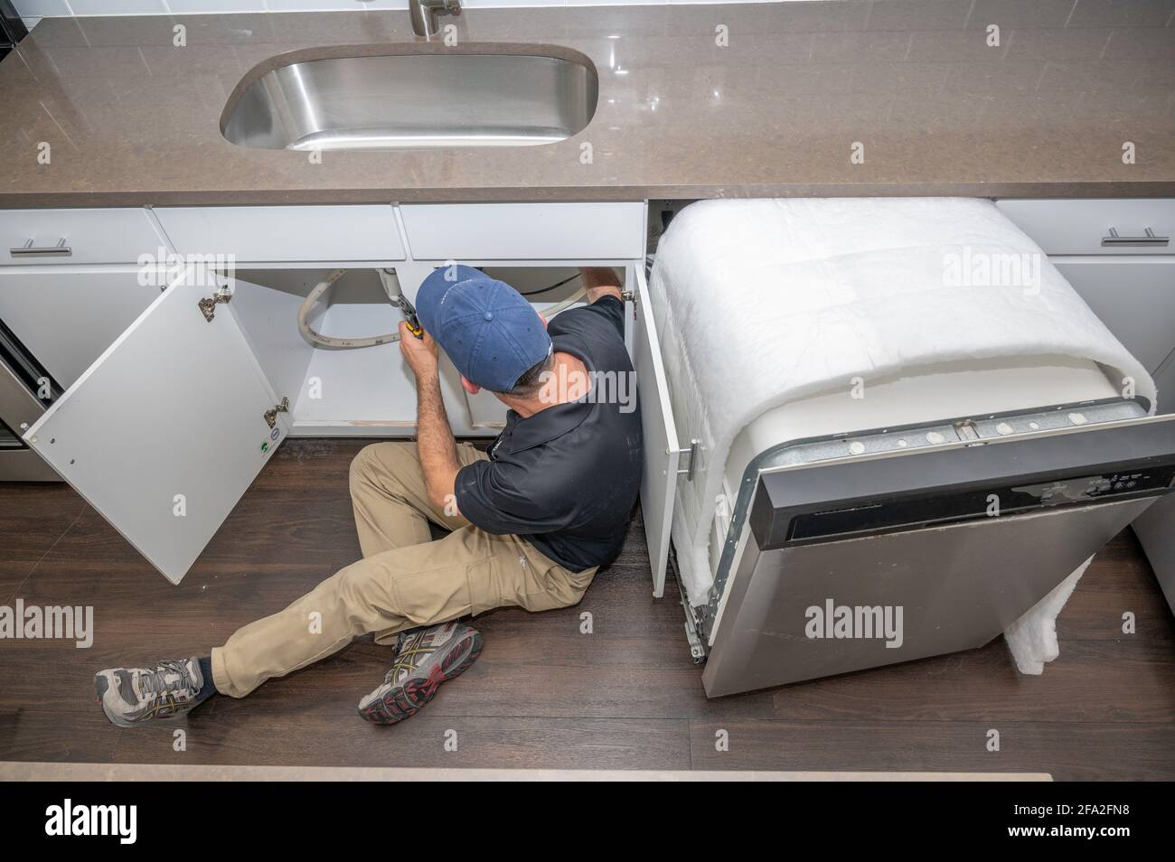 Appliance repairman working underneath a kitchen sink installing a