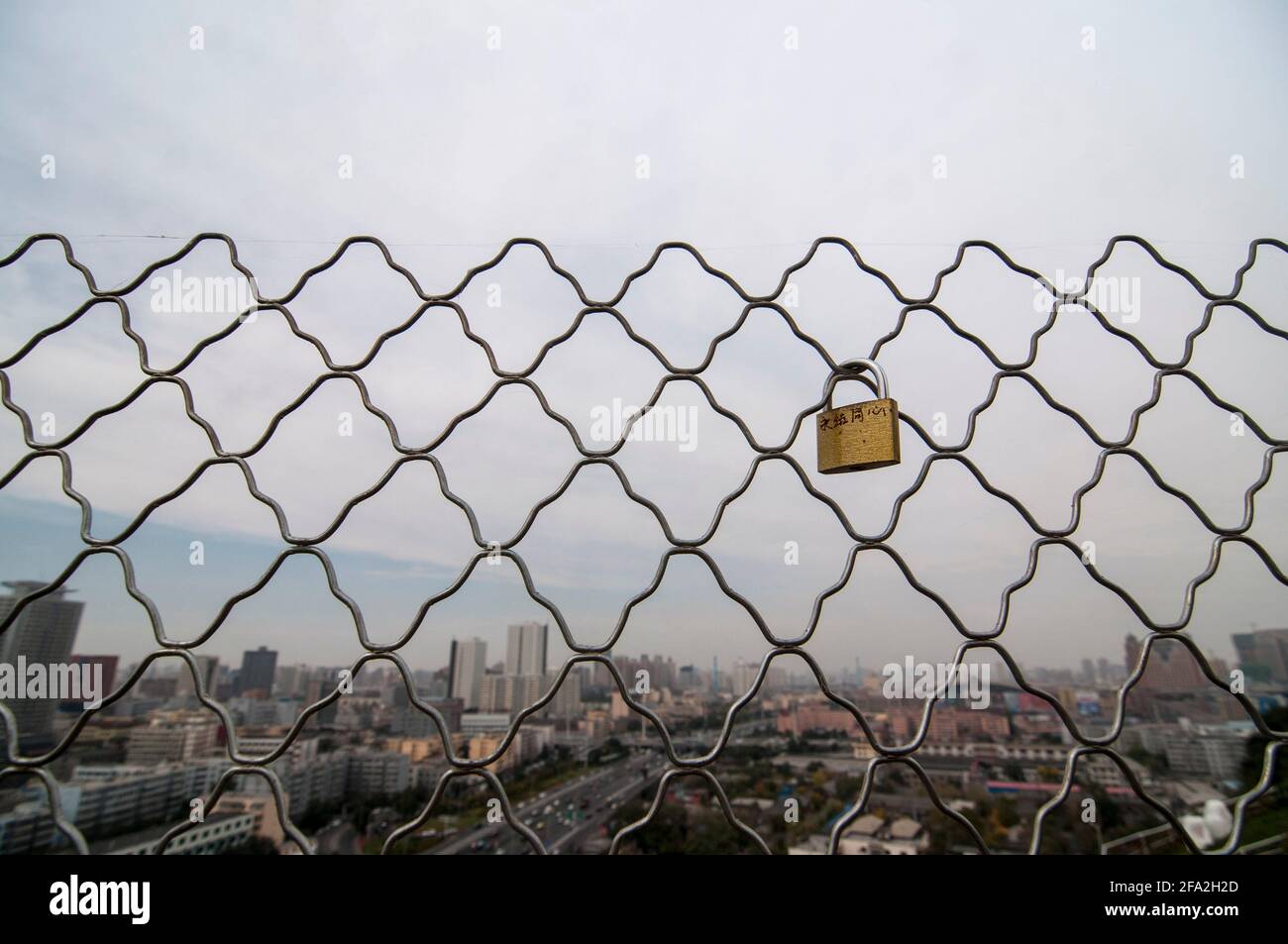 A padlock, used a lovelock is seen on a fence in front of the skyline with offices, residential high rise buildings and skyscrapers of the central district of Jiefang in Urumqi in Xinjiang, China, PRC.  © Time-Snaps Stock Photo