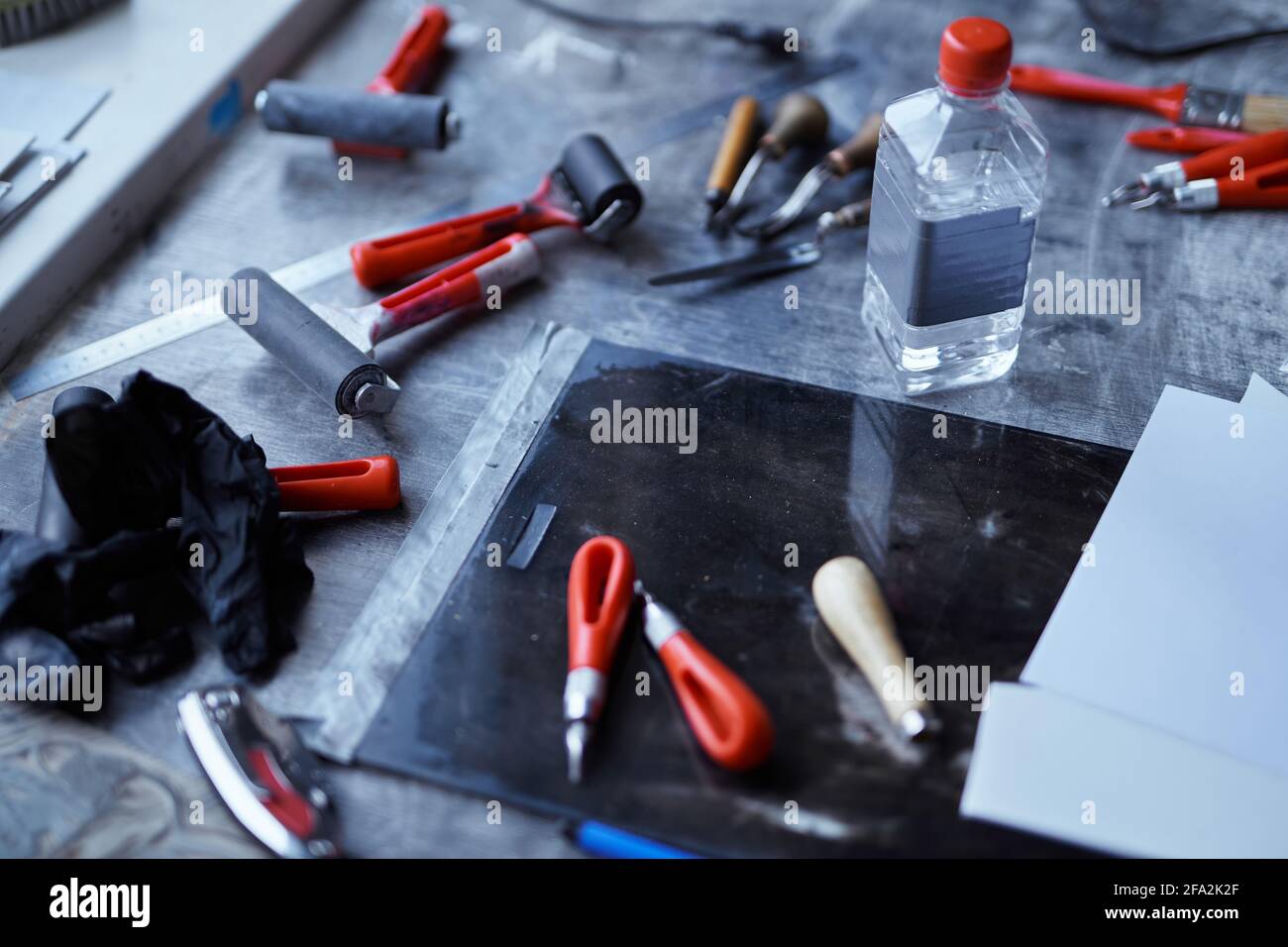 Linocut tools concept. Working tools in red and black colors on dark table  with copy space. Cutting instruments, ink roller and other tools for  linocut making. High quality photo Stock Photo 