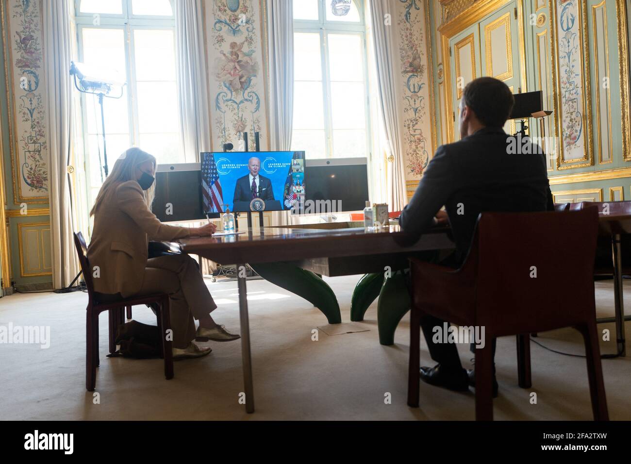 French President Emmanuel Macron listens to US President Joe Biden (on screen) speak during a virtual Earth Day Climate Summit, video conference call, at the Elysee Palace in Paris on April 22, 2021. President Joe Biden on April 22, 2021, sharply ramped up US ambitions on slashing greenhouse gas emissions, leading new pledges by allies at a summit he hopes brings the world closer to limiting climate change. Biden told a virtual Earth Day summit that the world's largest economy will cut emissions blamed for climate change by 50 to 52 percent by 2030 compared with 2005 levels. Photo by Romain Ga Stock Photo