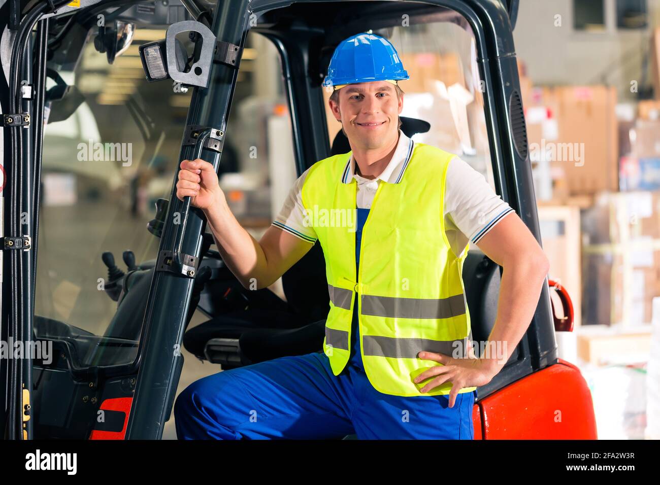 forklift driver in protective vest and forklift standing at warehouse ...