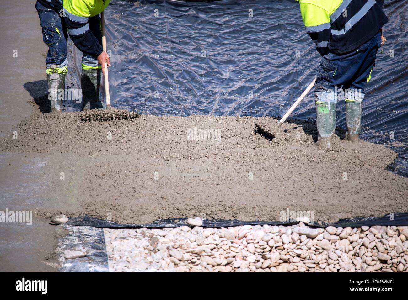 Two construction workers at work pouring a mixture on a floor with a plastic sheet. Stock Photo