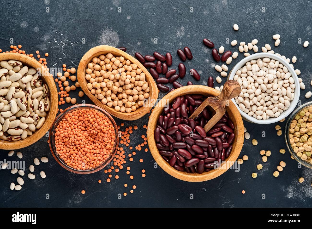 Legumes, red lentils, chickpea, red and white beans assortment in different bowls on dark black