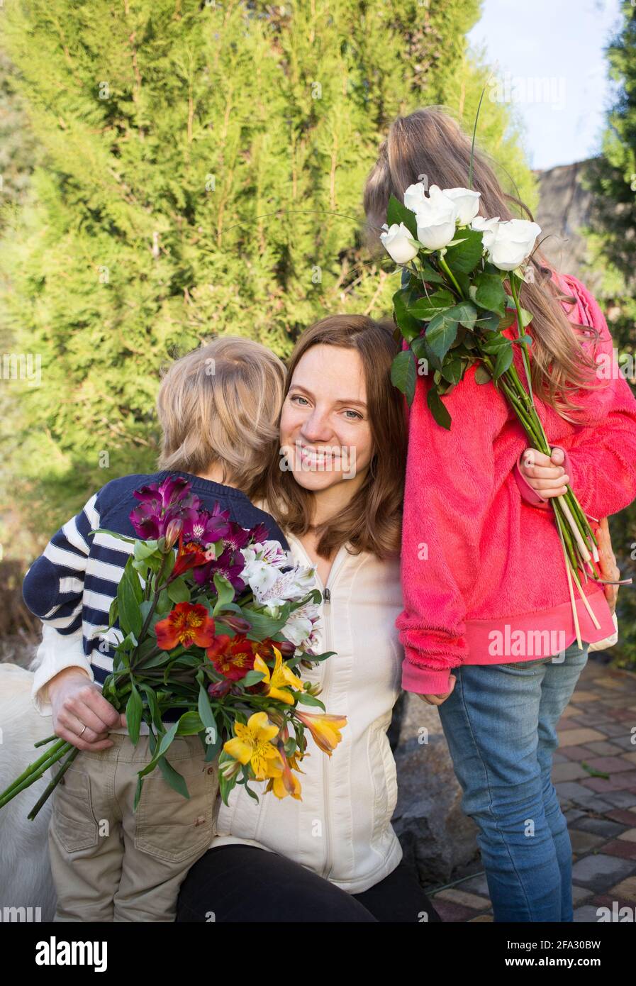 portrait of happy mother, whom unrecognizable children, boy and girl give 2 bouquets of flowers . Joyful emotions, positive, motherhood. Congratulatio Stock Photo