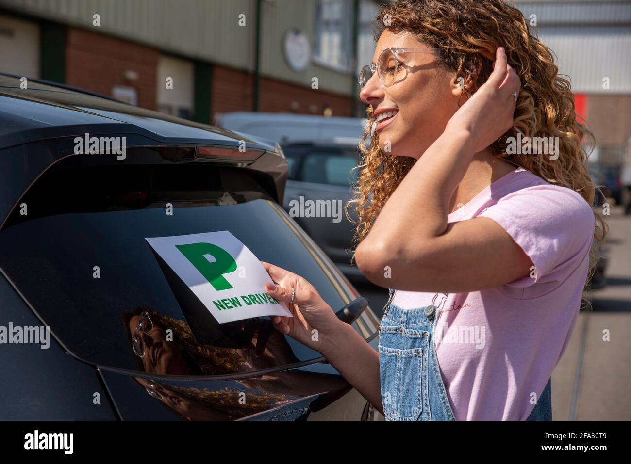 England, UK. 2021.  New driver, young attractive woman holding a green new driver sign to display on her car after passing the driving test. Stock Photo