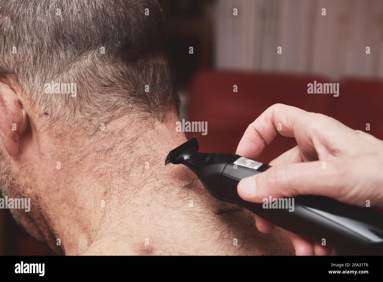 Wife cutting husbands hair at home with a haircut machine or hair clipper. Stock Photo