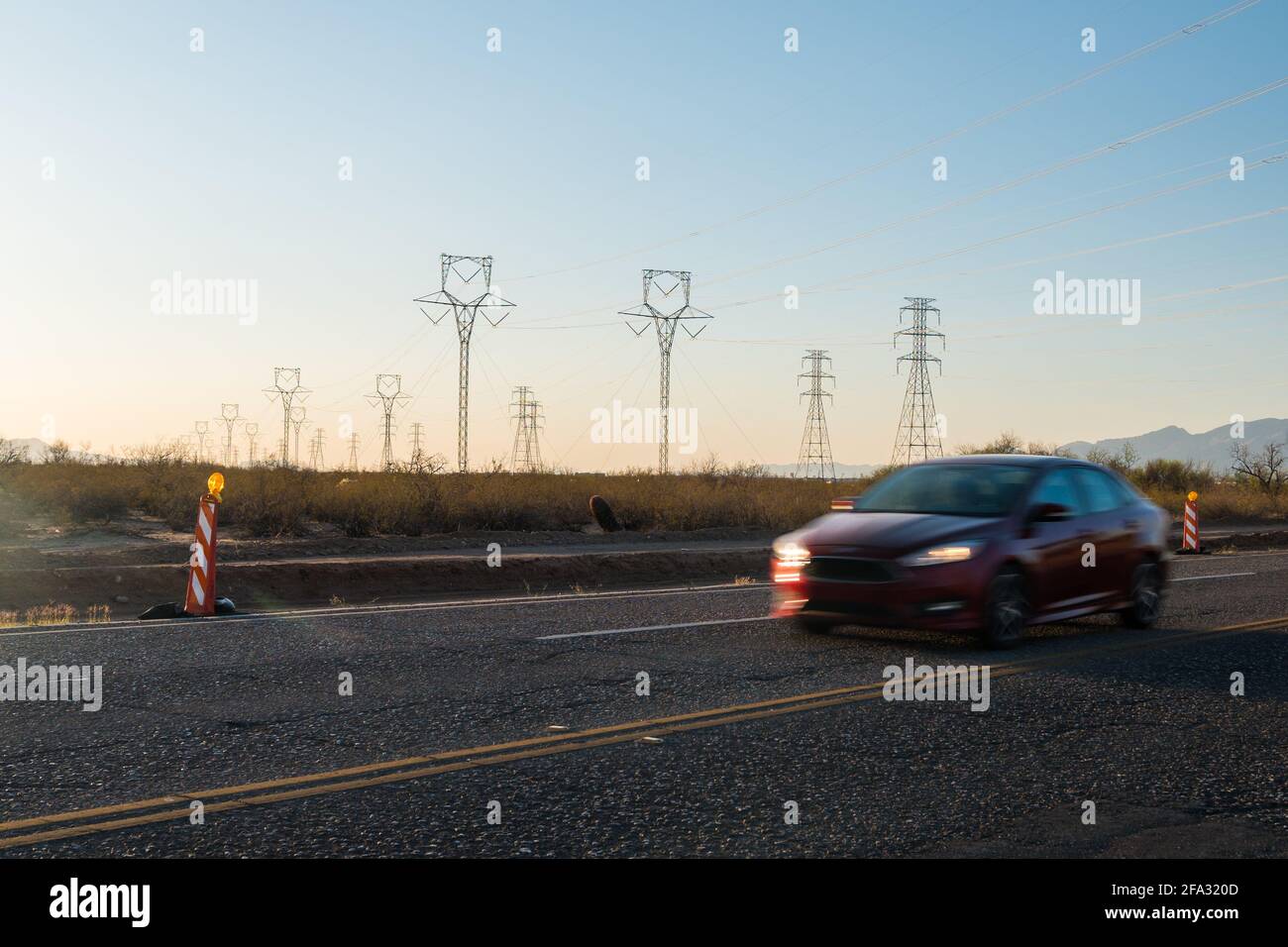 Electric pylons at sunset. Cars drive by on street.  Stock Photo