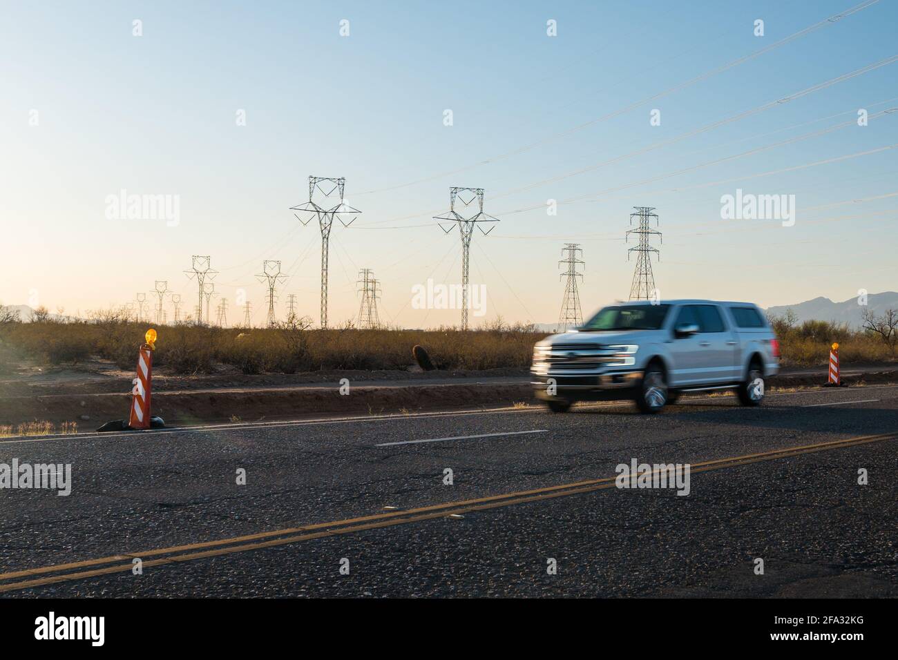 Electric pylons at sunset. Cars drive by on street.  Stock Photo