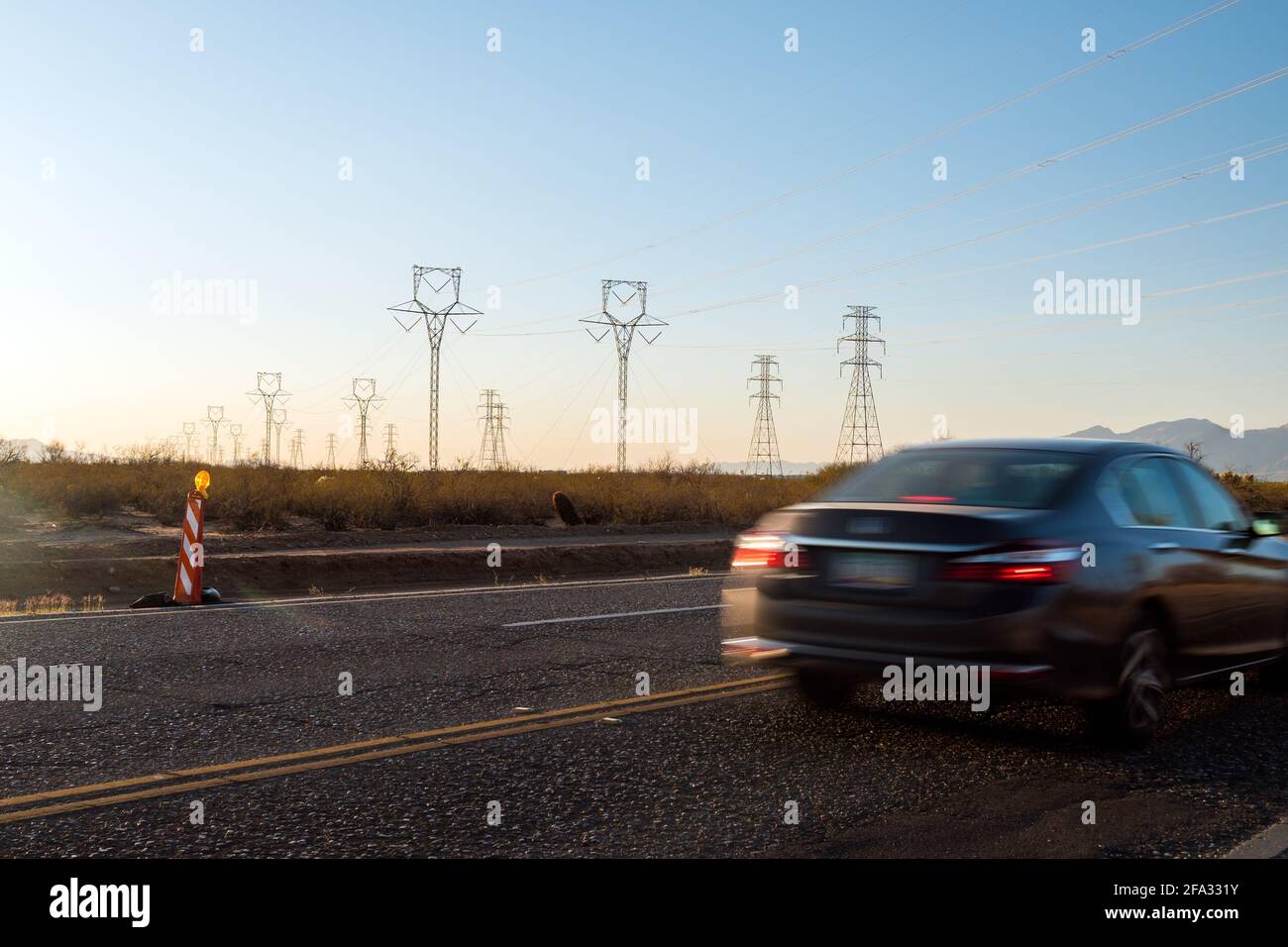 Electric pylons at sunset. Cars drive by on street.  Stock Photo