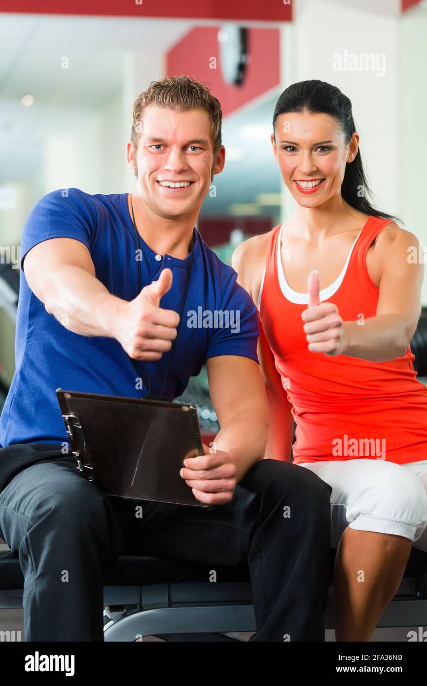 Woman with her personal fitness trainer in the gym exercising with ...