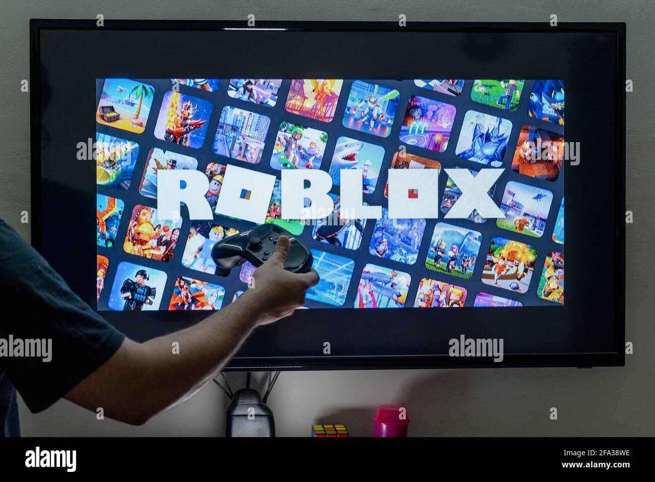 man with a controller standing in front of a PC console TV screen with a steam  controller playing popular free to play game Roblox Stock Photo - Alamy