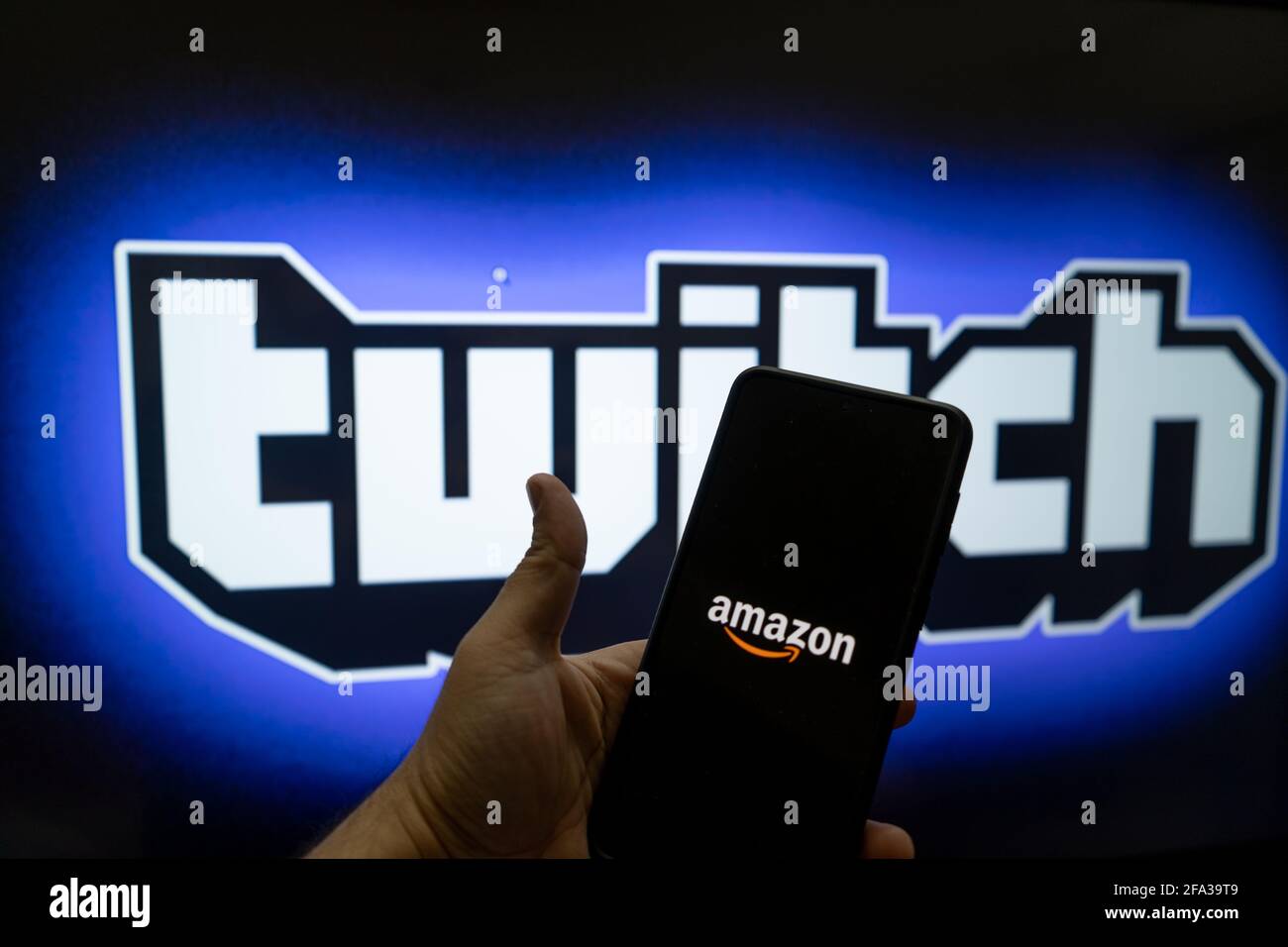 man holding mobile phone with amazon logo and twitch streaming platform  name and logo in the background showing this platform with full time  earning Stock Photo - Alamy