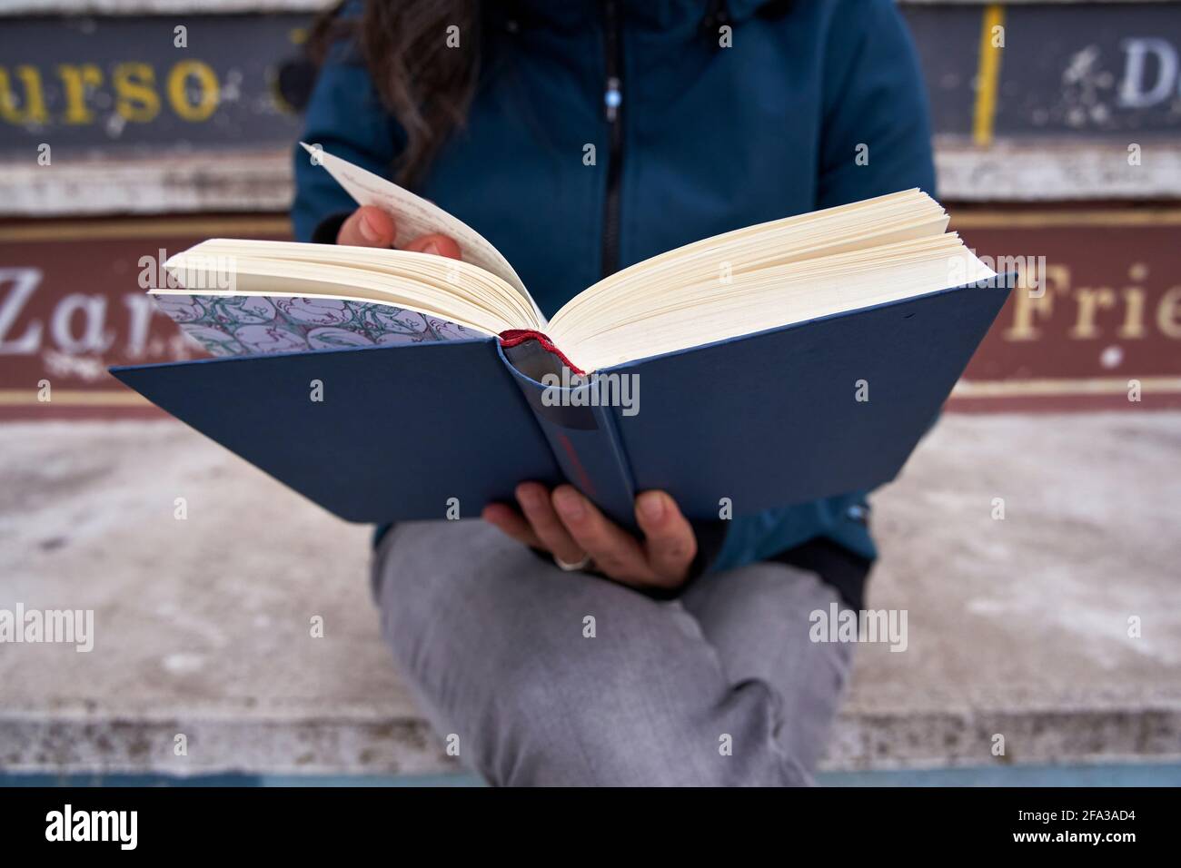 Detail of an open book being held by a woman, cropped out of focus. Stock Photo
