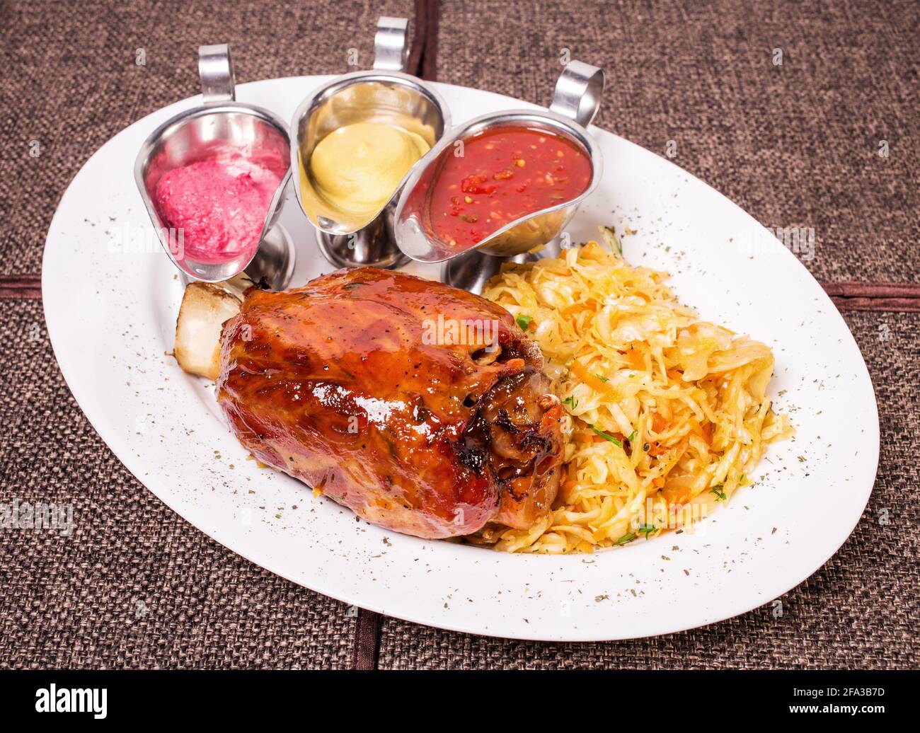 Baked pork knuckle with sauerkraut and various sauces in italian style. Plate located on a brown