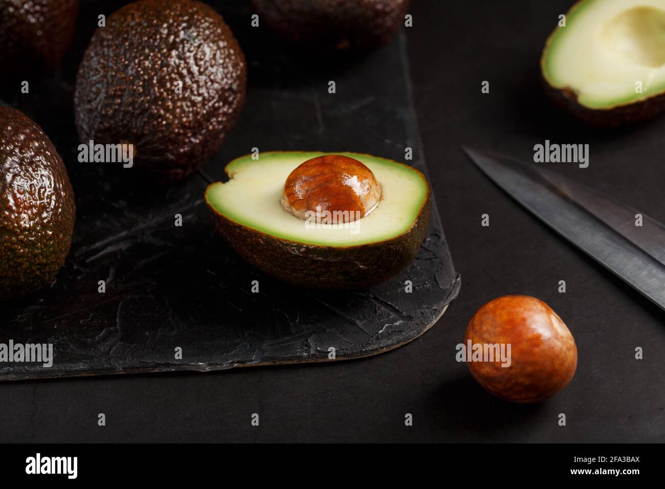Sliced and whole organic avocado Hass with a knife on a black