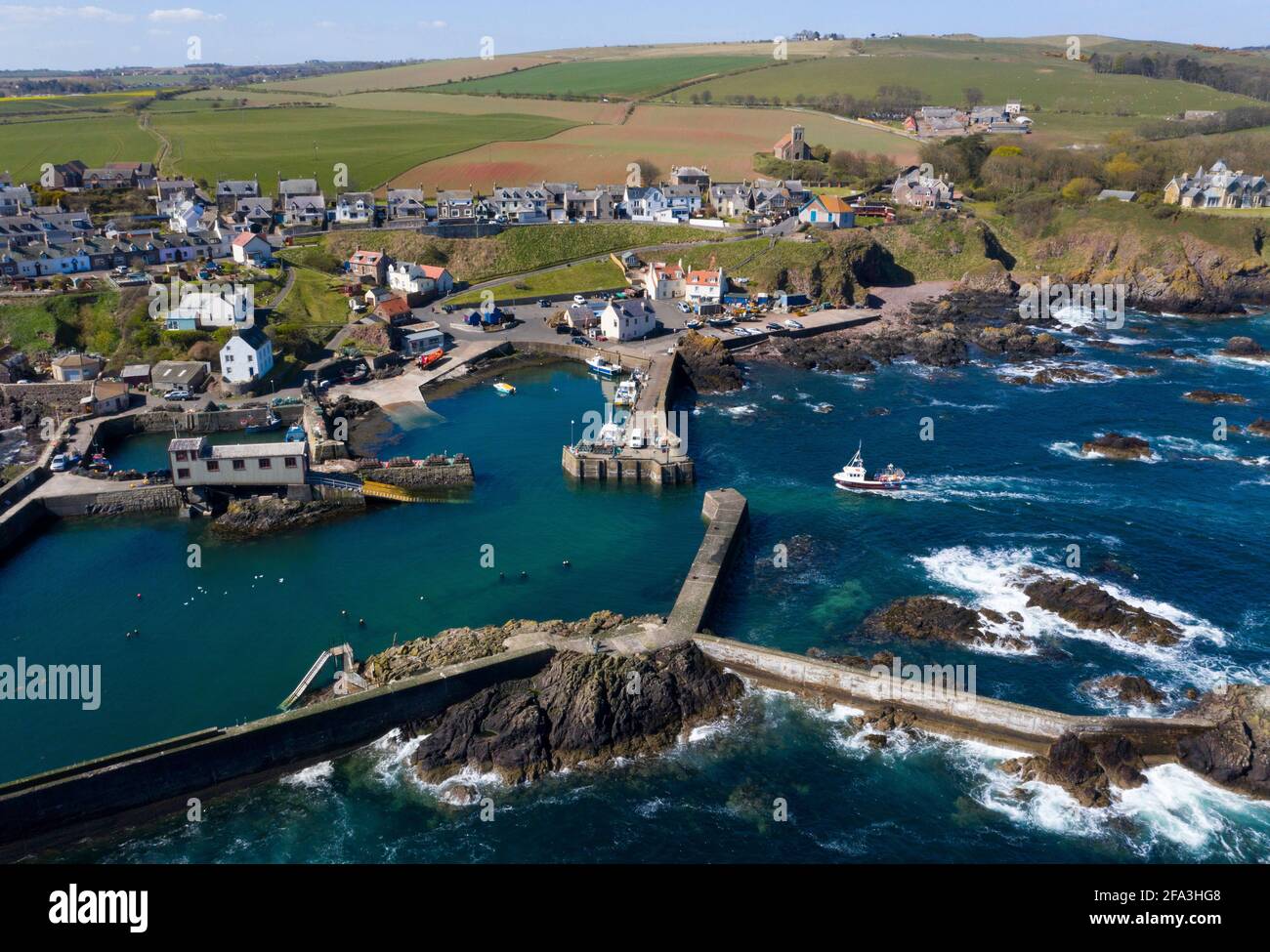 Aerial view shows a fishing vessel returning to St Abbs harbour on the Berwickshire coast, Scotland, UK. Stock Photo
