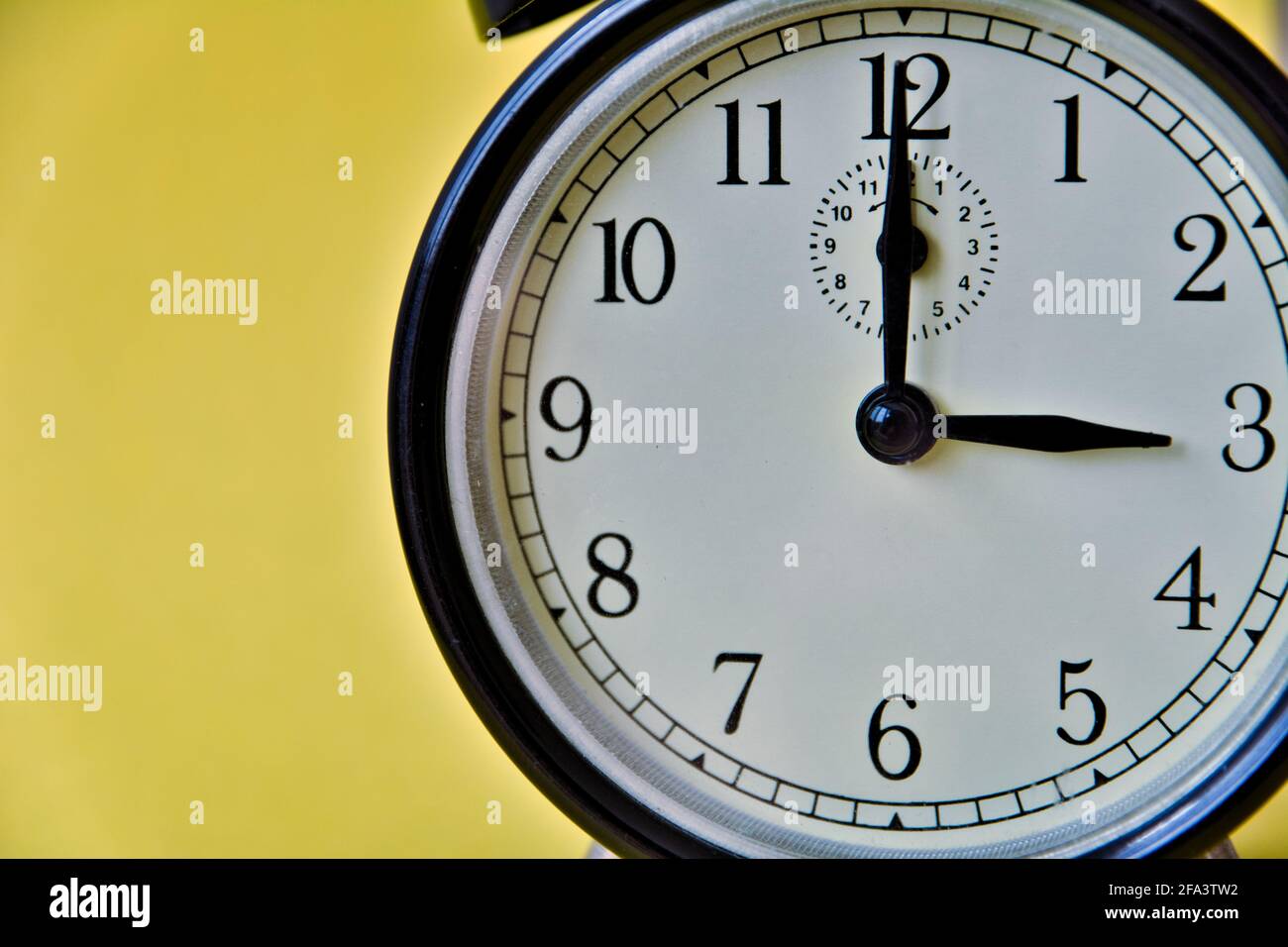 Shot of vintage retro analog clock on yellow background showing 3 o