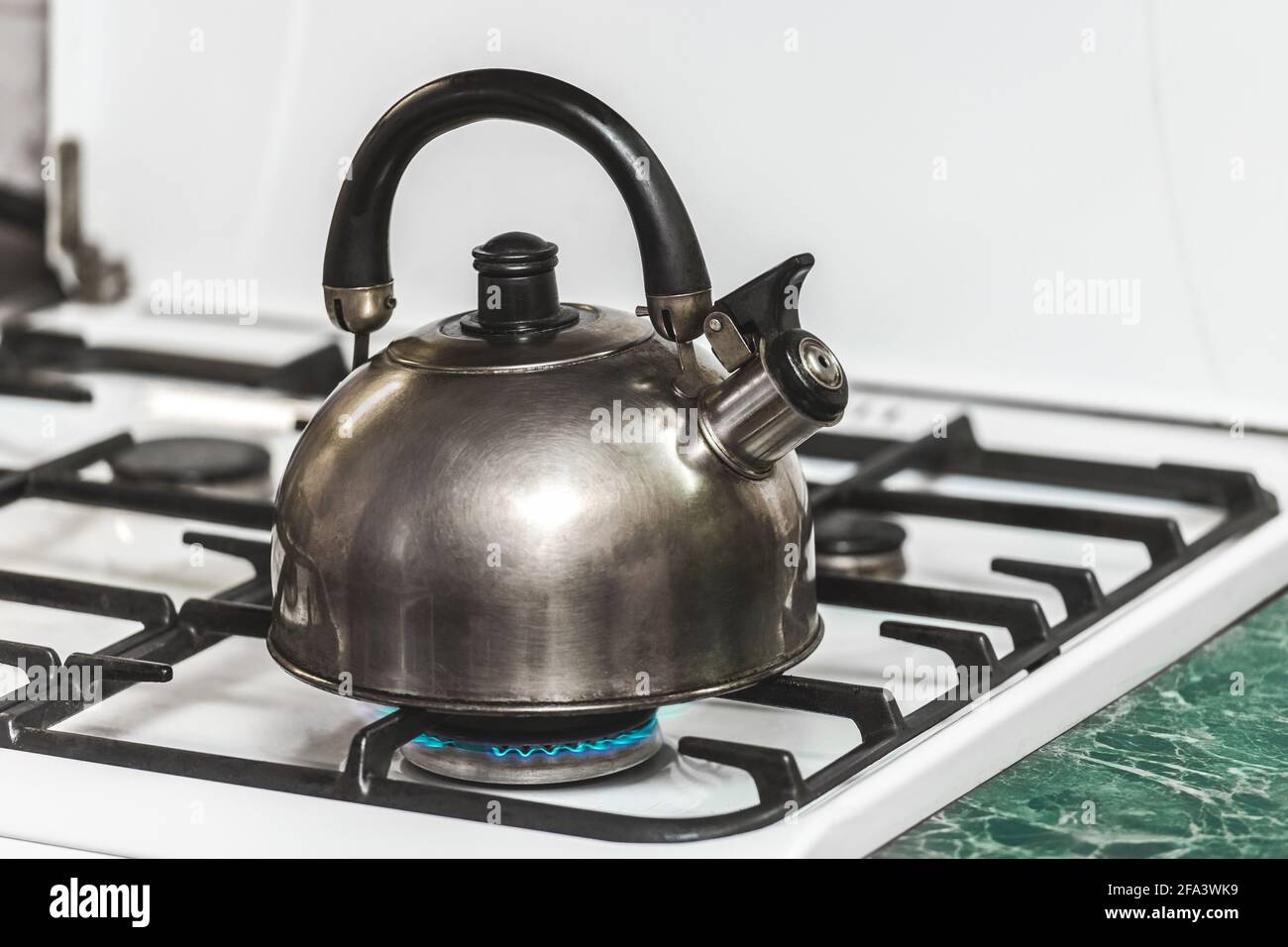 A metal dark kettle with a whistle heats the water to a boil on a gas