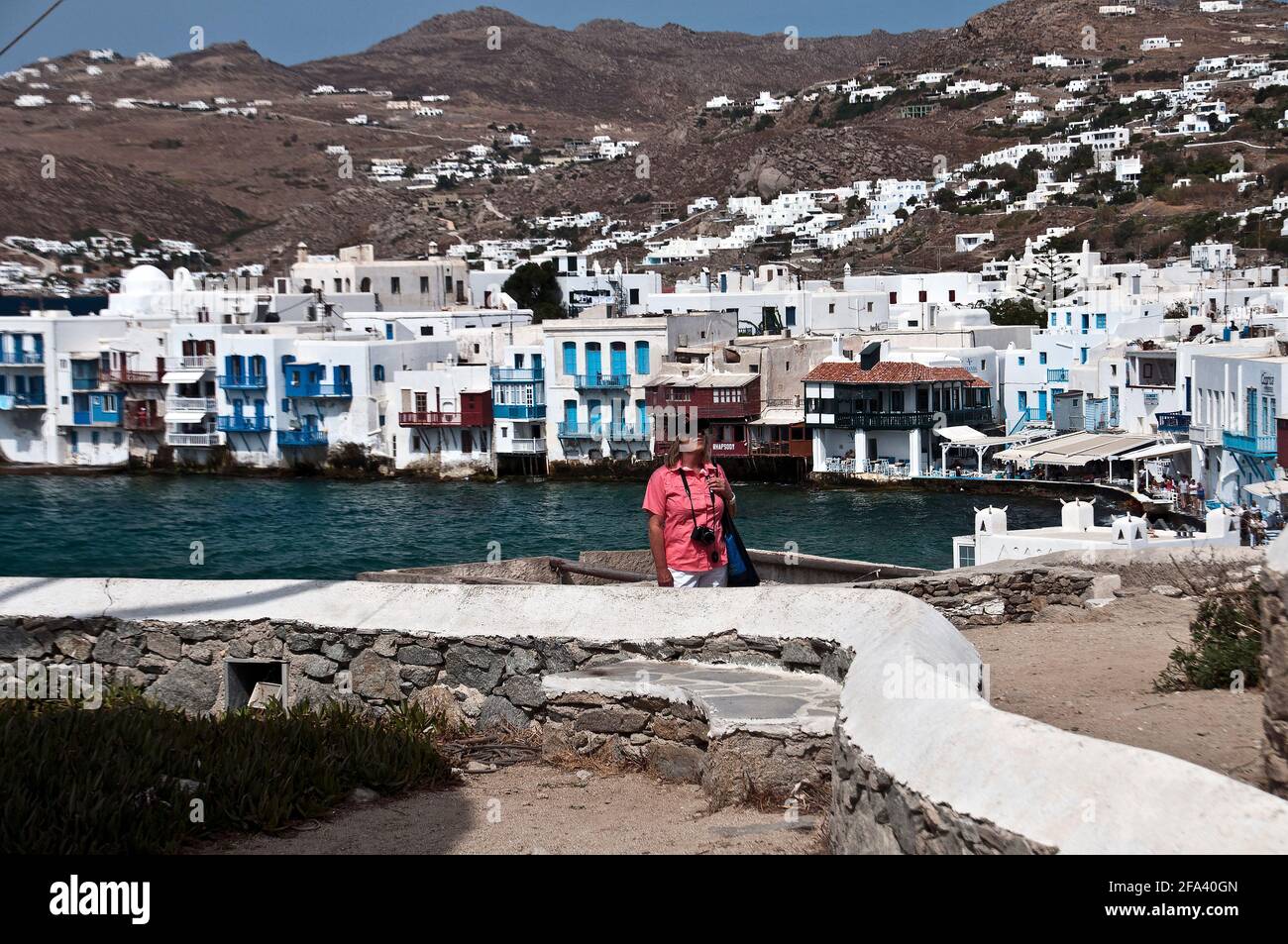 Female tourist in pink shirt, Mykonos Harbor and Mykonos in background Stock Photo
