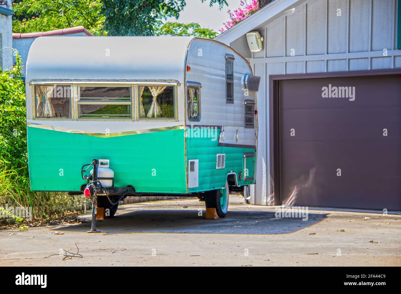 Turquoise and white vintage camper trailer parked beside garage door Stock Photo