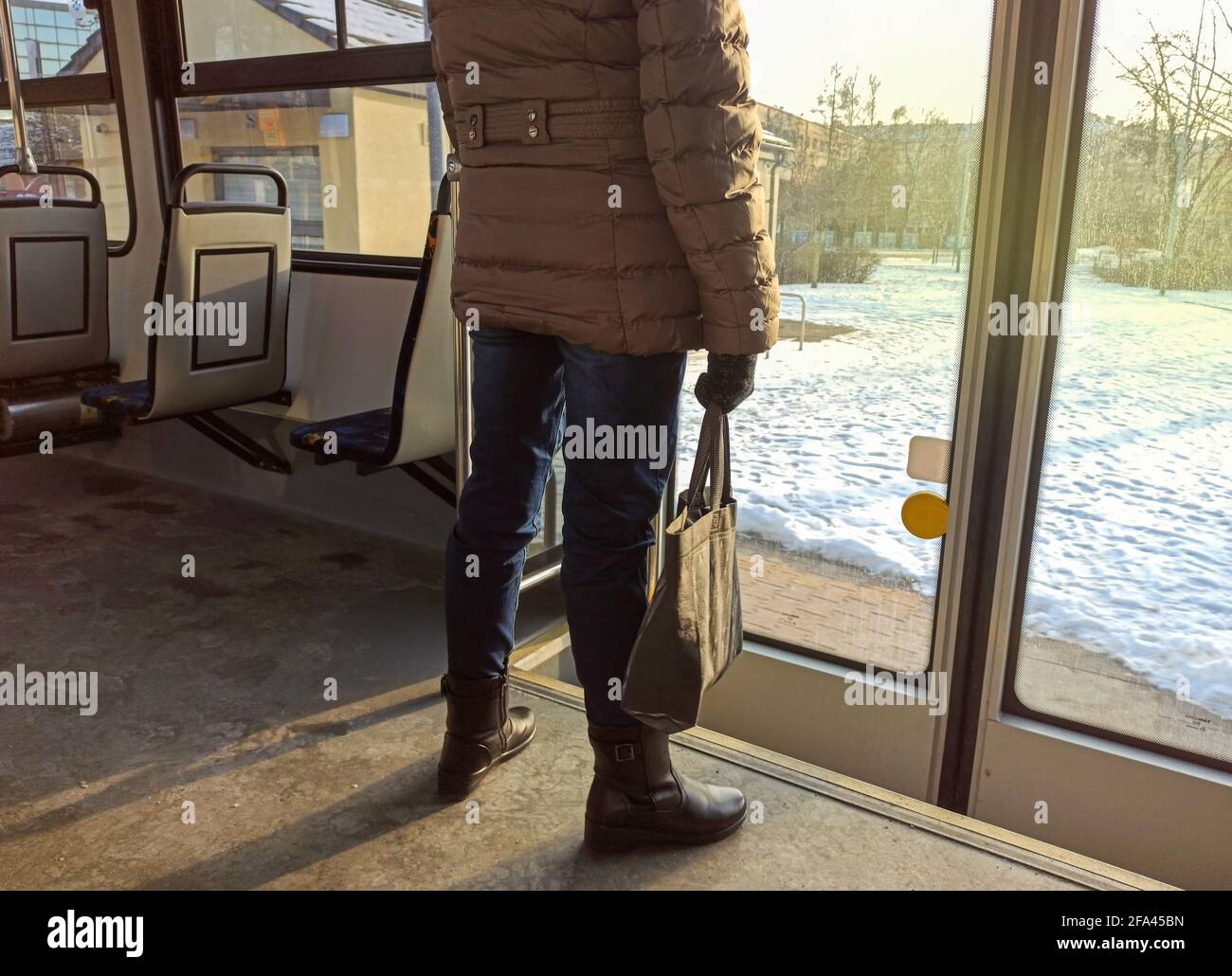 Rear side of a Woman passenger with jeans and coat jacket with hand bag standing in an empty bus during winters. Female traveling and waiting to exit Stock Photo