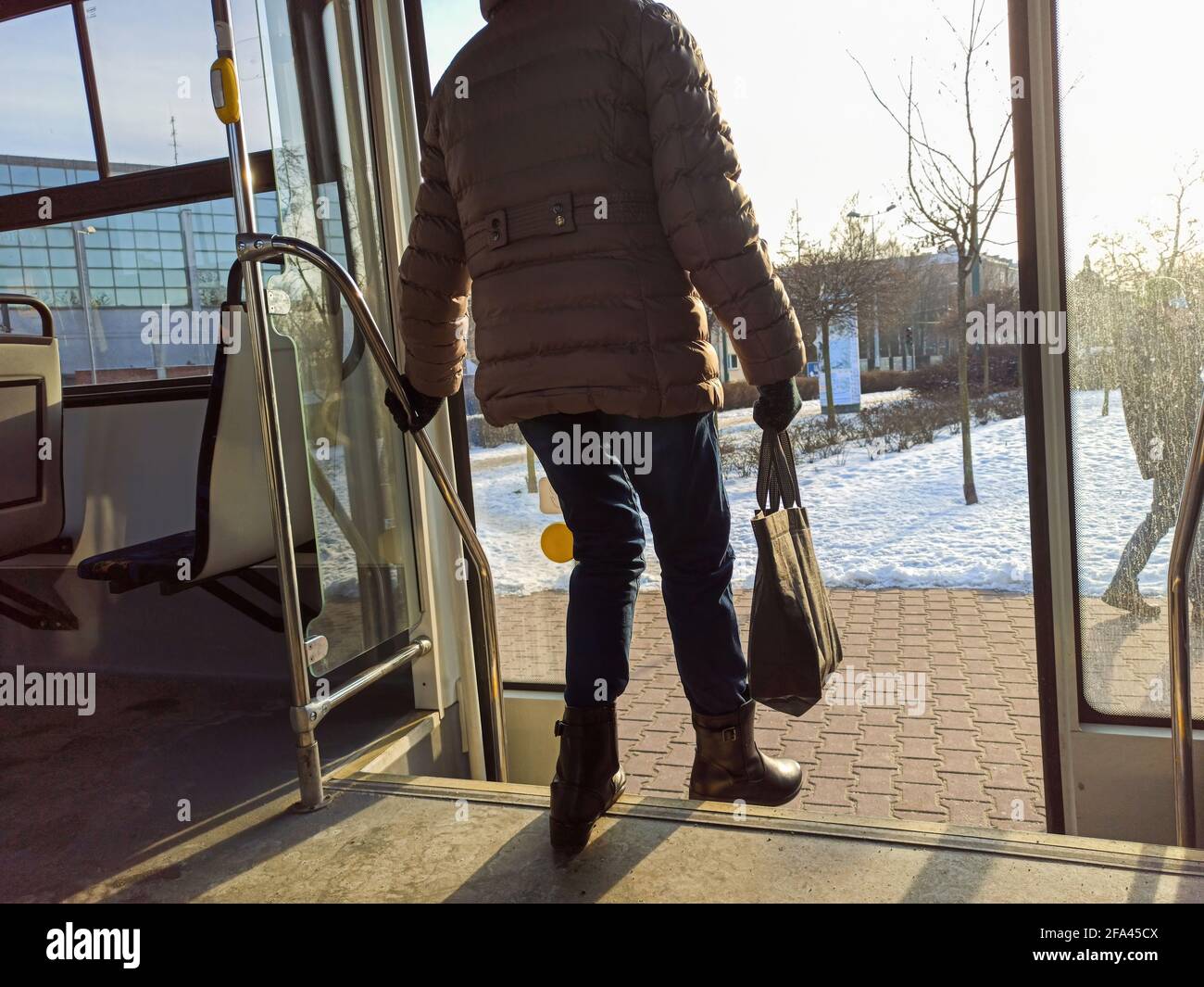Woman passenger with jeans and coat jacket with hand bag getting off the bus during winters. Female deboarding, stepping down or exiting from public t Stock Photo