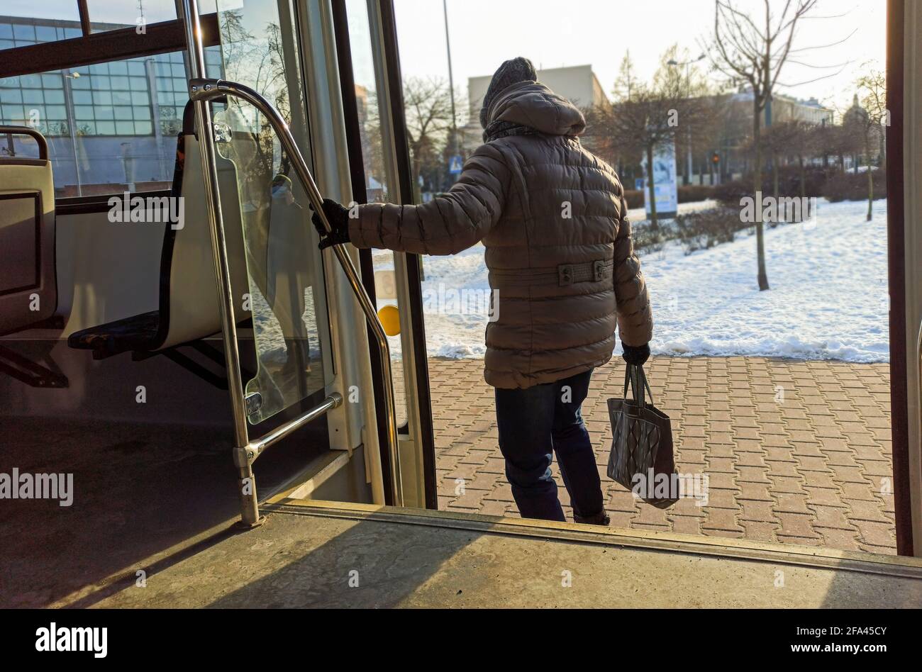 Woman passenger with jeans and coat jacket with hand bag getting off the bus during winters. Female deboarding or exiting from public transportation a Stock Photo