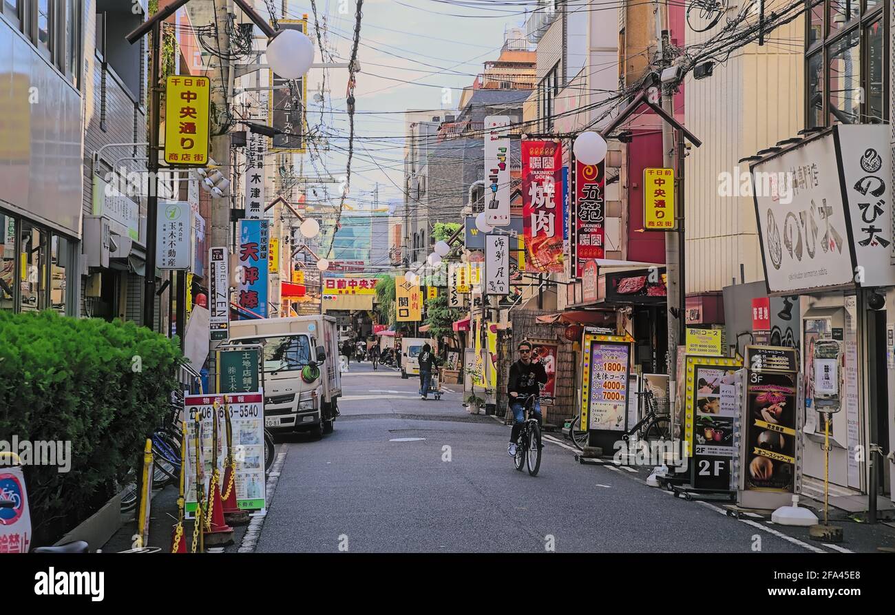 Osaka, Japan - November 5 2020: Vibrant signs line a side street in central Osaka on a hazy autumn morning, with several pedestrians and a cyclist vis Stock Photo