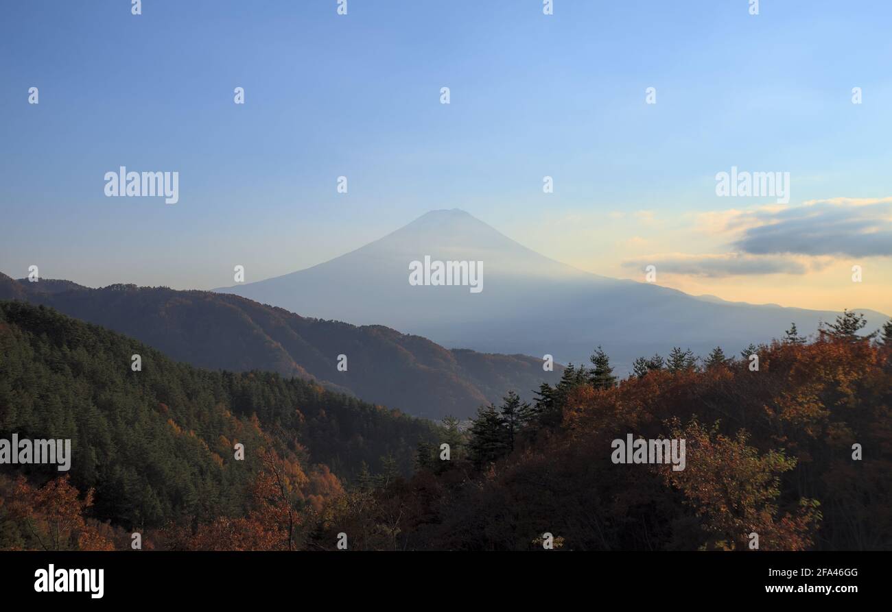 Panoramic view of Mount Fuji from behind a few forested mountains in the late afternoon on a sunny day Stock Photo