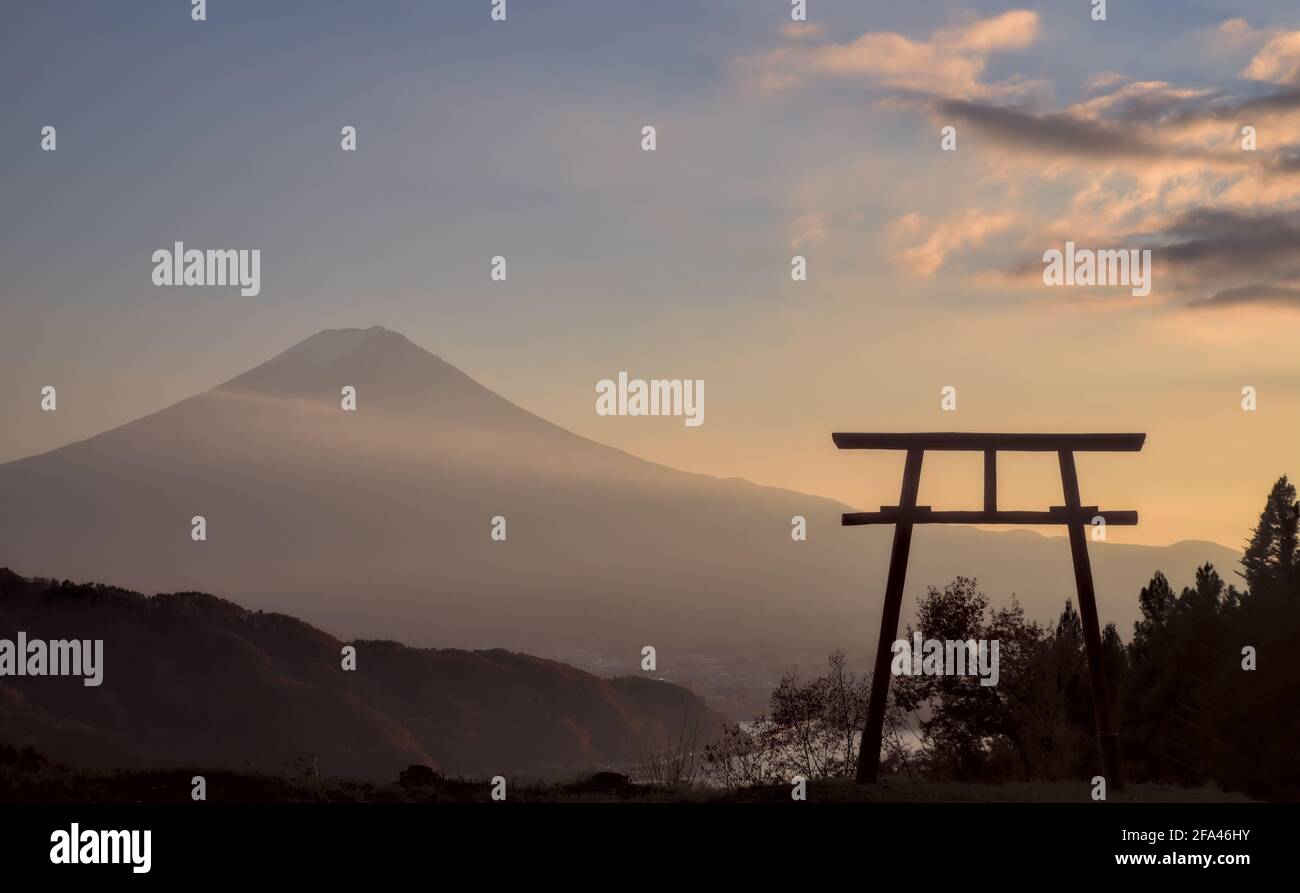 Late afternoon view of a torii gate and Mount Fuji under a partly-cloudy blue and yellow sunset sky Stock Photo