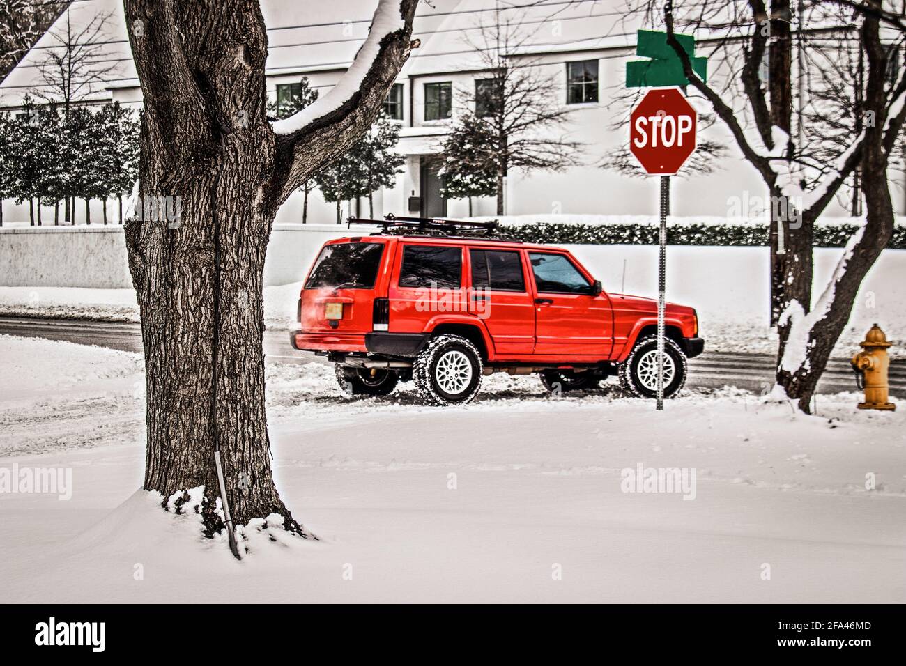 Four wheel drive SUV stopped at stop sign on snowy day getting ready to turn onto cleared roat from road in upscale neighborhood. Stock Photo