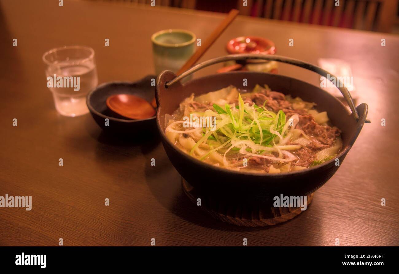 A bowl of houtou noodles and accompanying tableware on a wooden table inside a restaurant Stock Photo
