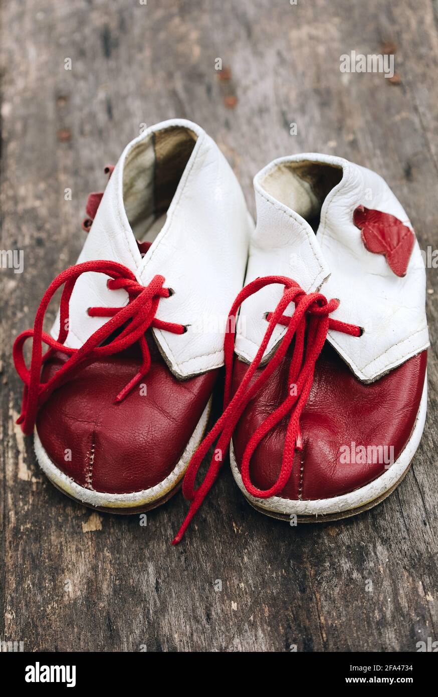 Cute leather red and white baby boots with laces, vintage retro fashion, first foot wear for child on wooden background Stock Photo