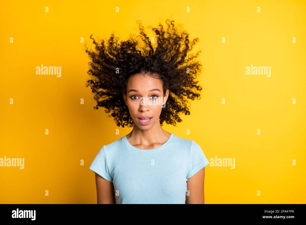 Photo of impressed funny dark skin curly woman dressed blue t-shirt air  blow hair isolated yellow color background Stock Photo - Alamy