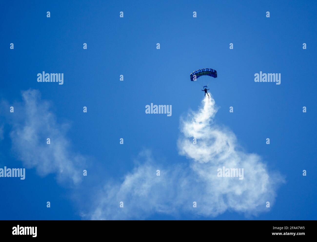 Red Devils Parachute Display Team descend with a long smoke trail over Salisbury Plain military training grounds under a cloudless bright blue sky Stock Photo