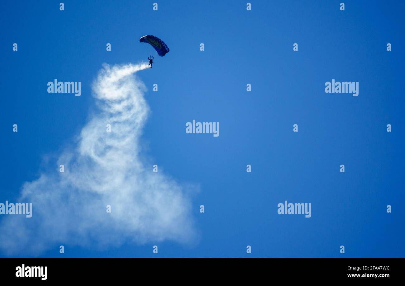 Red Devils Parachute Display Team descend with a long smoke trail over Salisbury Plain military training grounds under a cloudless bright blue sky Stock Photo