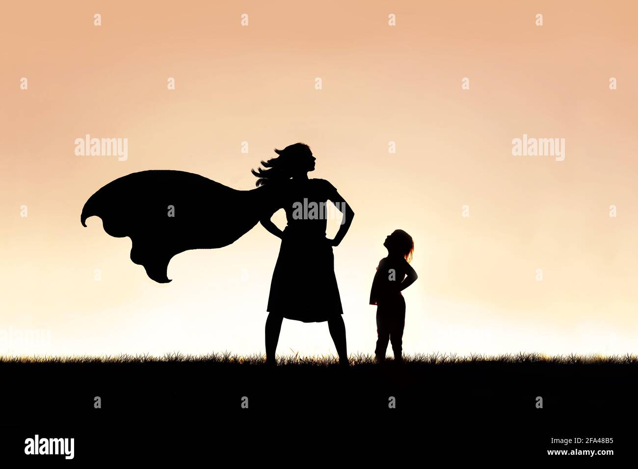 The silhouette of a strong, beautiful caped super hero woman stands isolated against a sunset in the sky background. Stock Photo