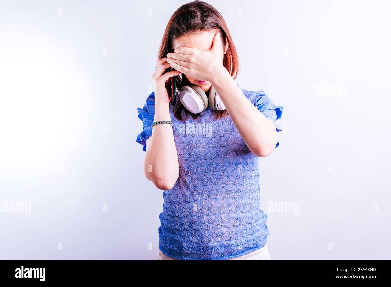 beautiful young woman wearing headphones receiving bad news by cell phone with hand on face Stock Photo