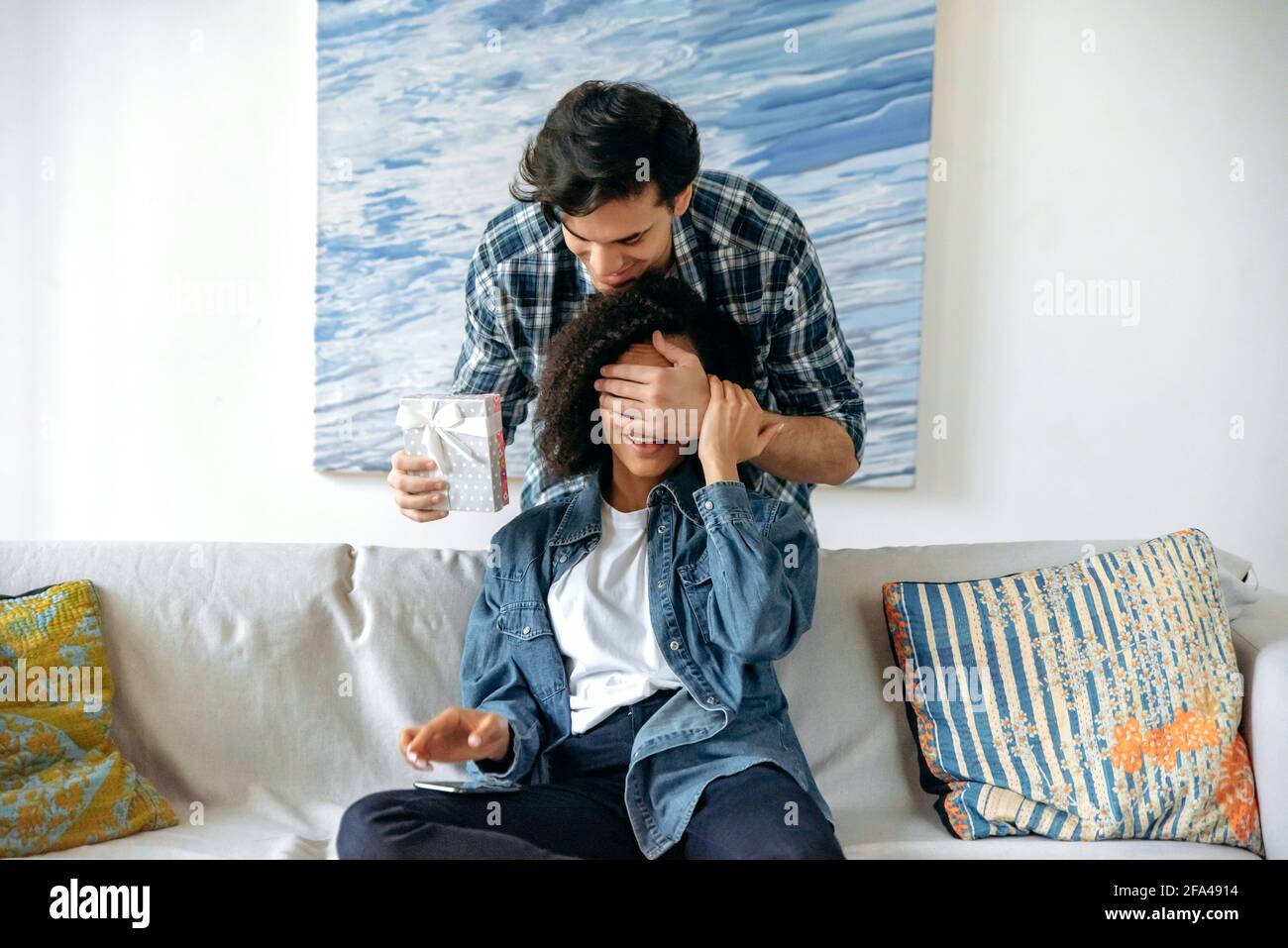 Romantic relationship of young couple. Attentive, loving caring guy in casual wear, covering eyes to girlfriend with his hand, getting ready to give her an relationship anniversary or birthday gift Stock Photo