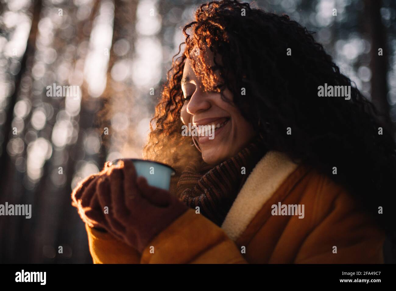 Happy young woman holding cup of tea standing in forest during winter Stock Photo