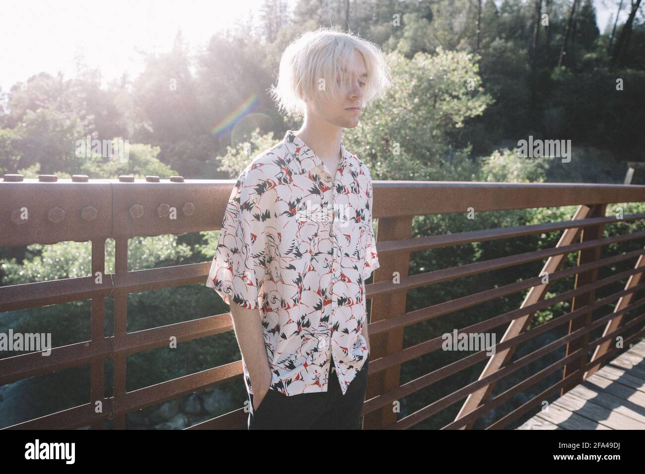 Slim Teen Stands Hands in Pockets Backlit on Bridge looking Serious Stock Photo
