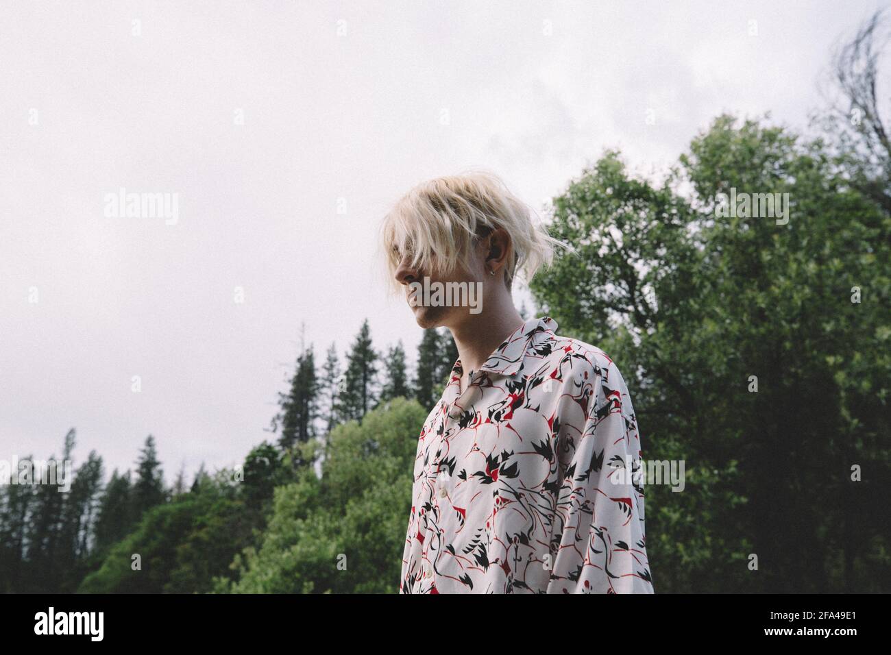 Low Angle Of Blonde Teen Standing Against Trees and Sky Stock Photo
