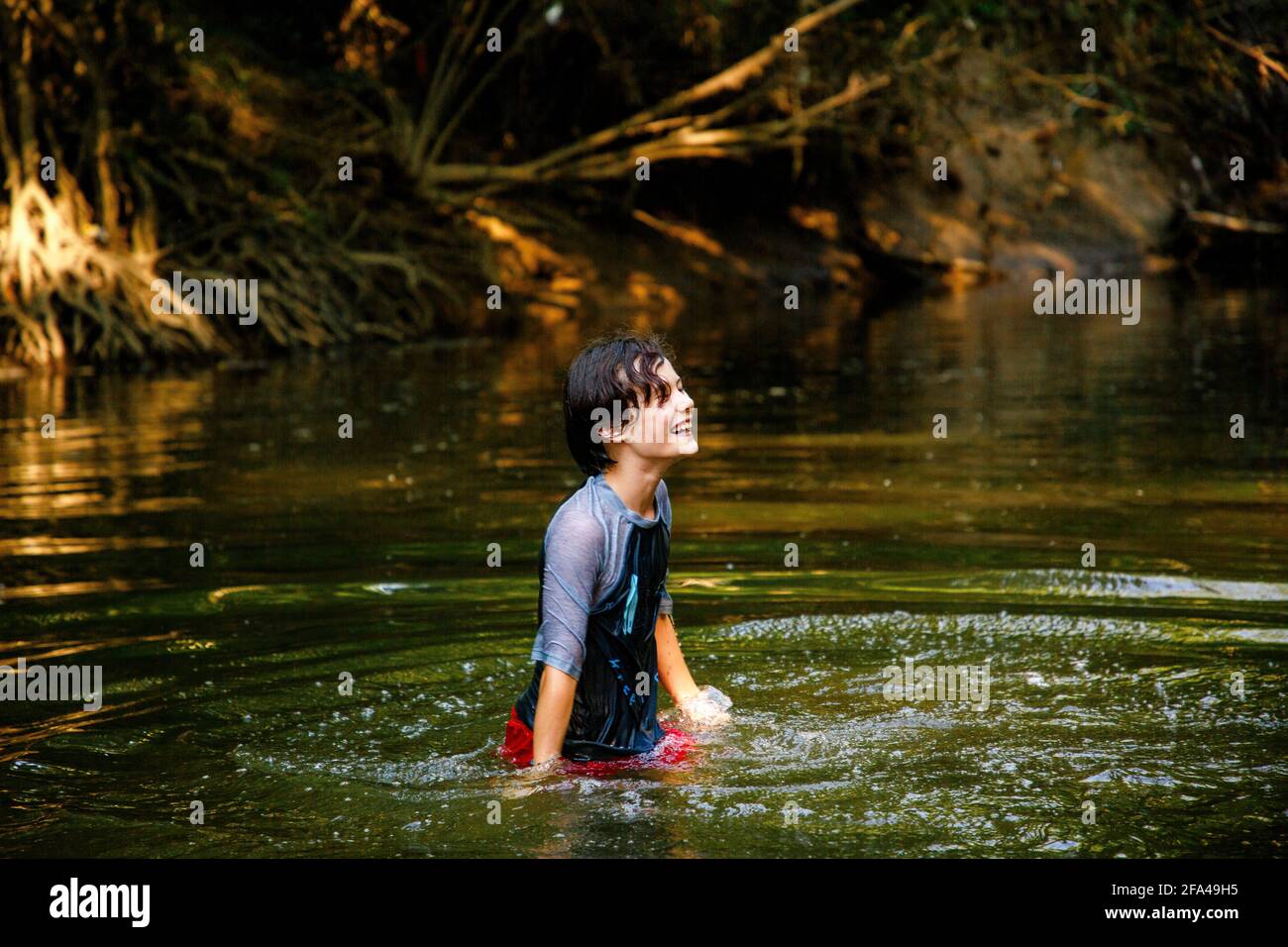 A happy boy plays in a river in golden sunlight in summertime Stock Photo