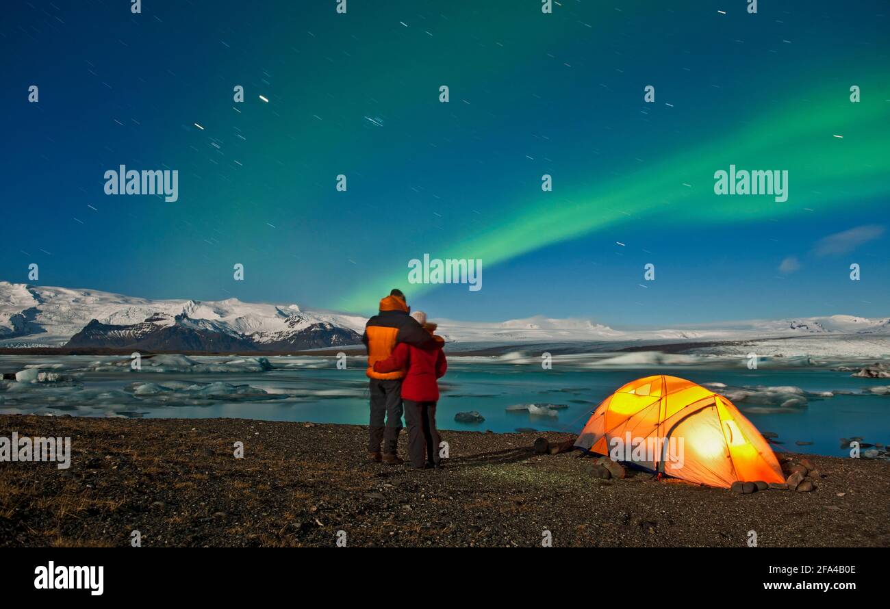 couple outside of their tent looking at Northern Lights in the sky Stock Photo