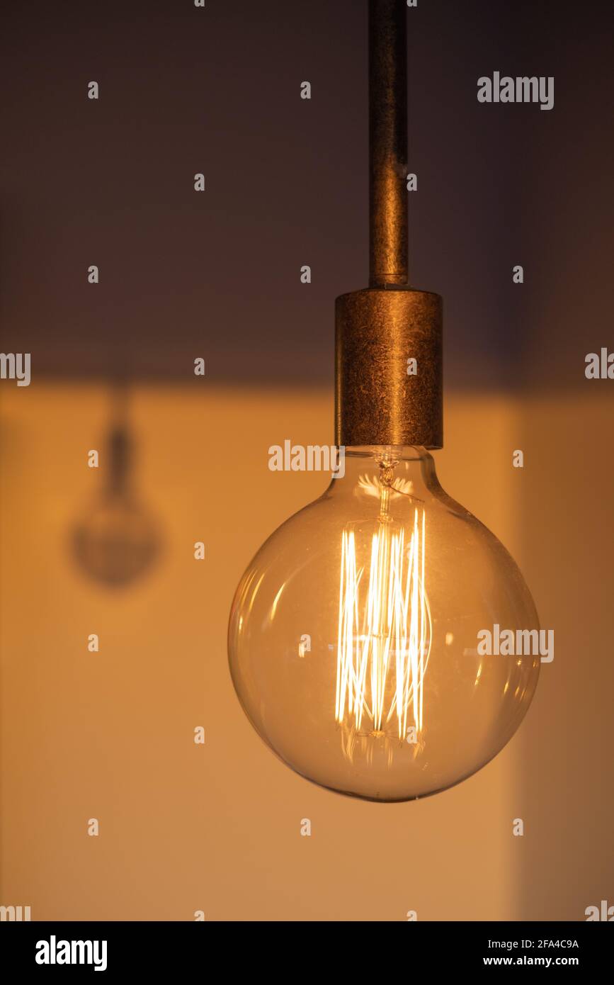 Glowing Light Bulb Hanging From the Ceiling and its Shadow Stock Photo