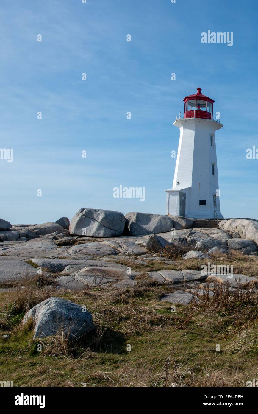 A rocky footpath among large rock boulders leading to a tall round vintage white tower lighthouse with a red watchtower at the top near the Atlantic Stock Photo