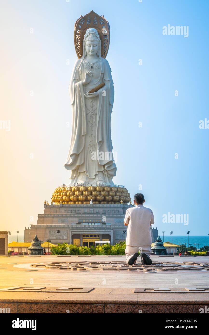 Unrecognizable monk praying in front of 108m high Guanyin of the South Sea statue of Nanshan Buddhism cultural park temple at sunrise in Sanya in Hain Stock Photo